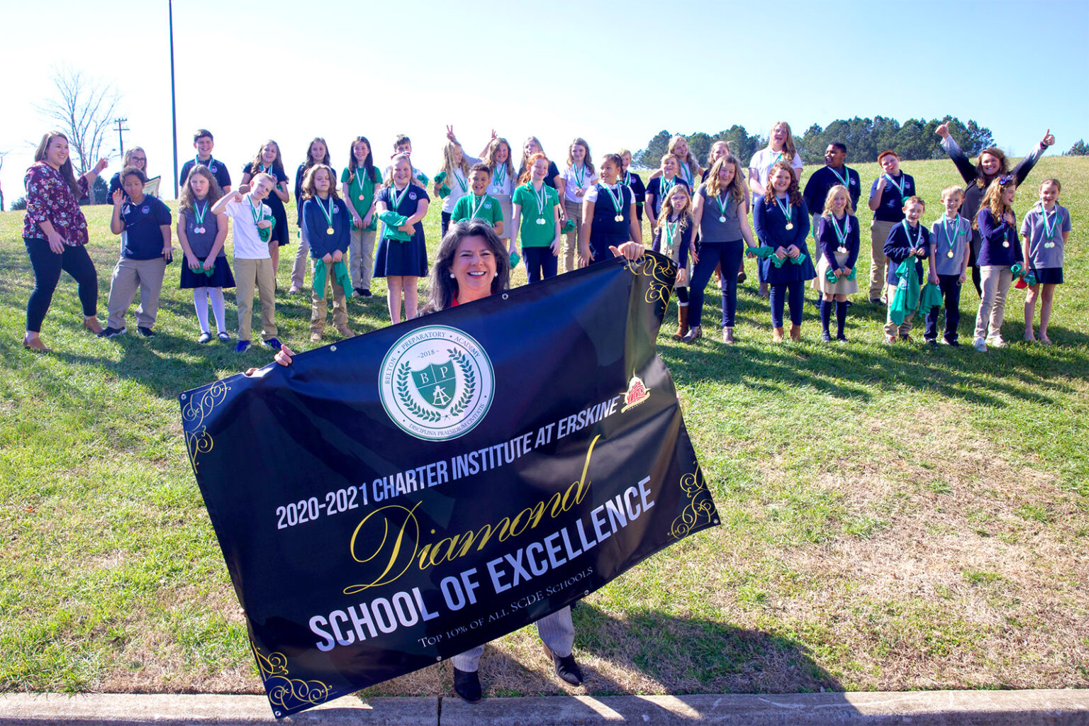 A teacher holding up a banner for Belton Preparatory Academy being a diamond school of excellence, with her students and fellow teachers behind her