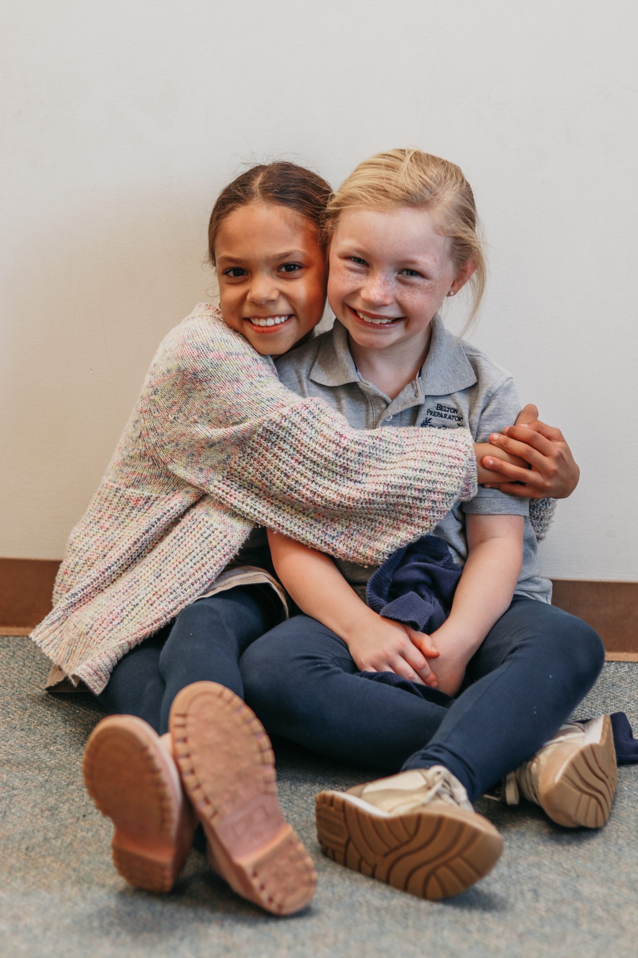 Two young students hugging while seated on the floor