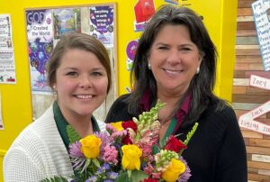 Teacher Megan Patterson smiling holding a bouquet of flowers that she received from the women next to her