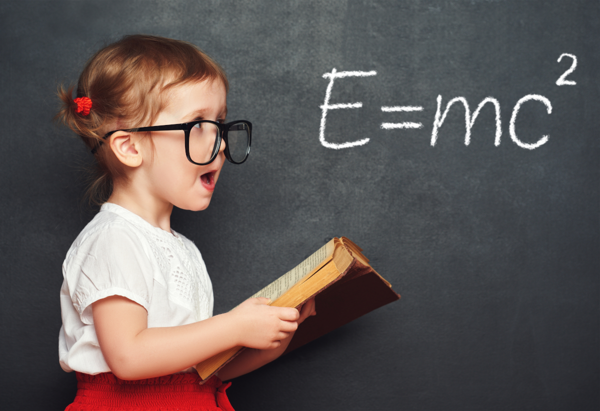 A young girl in front of a chalkboard with E-mc Squared on it in chalk