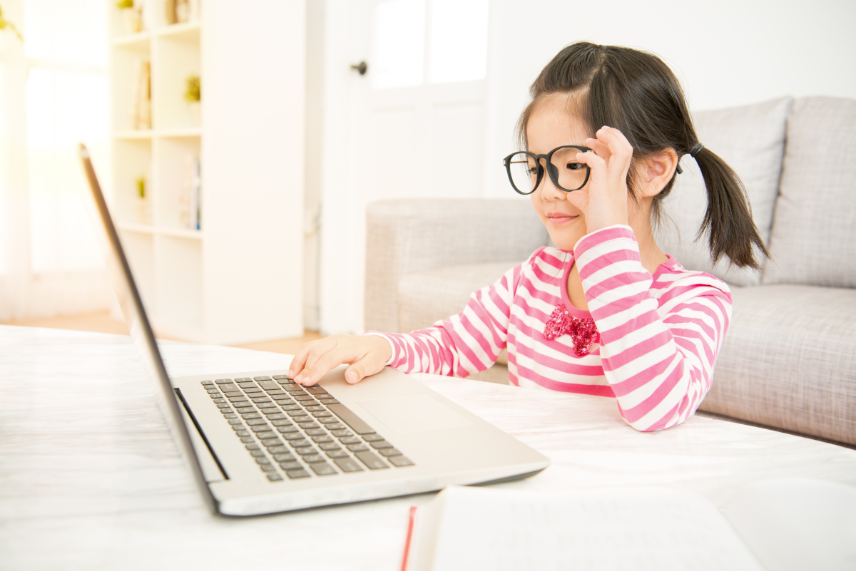 A young girl wearing glasses looking at a laptop