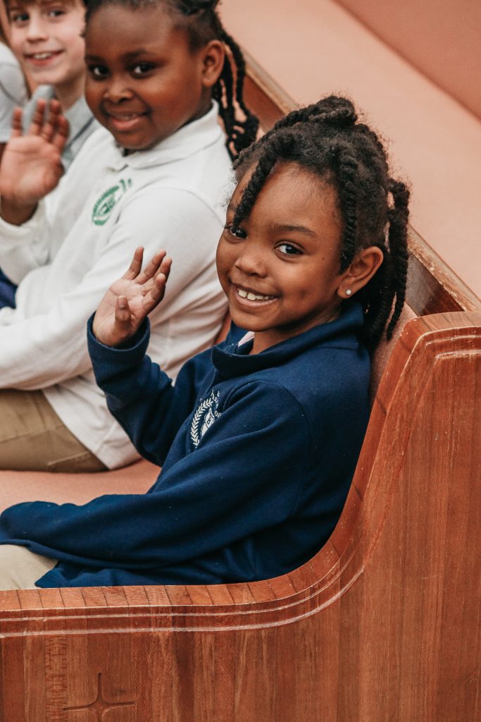 Students sitting in pew smiling and waving.